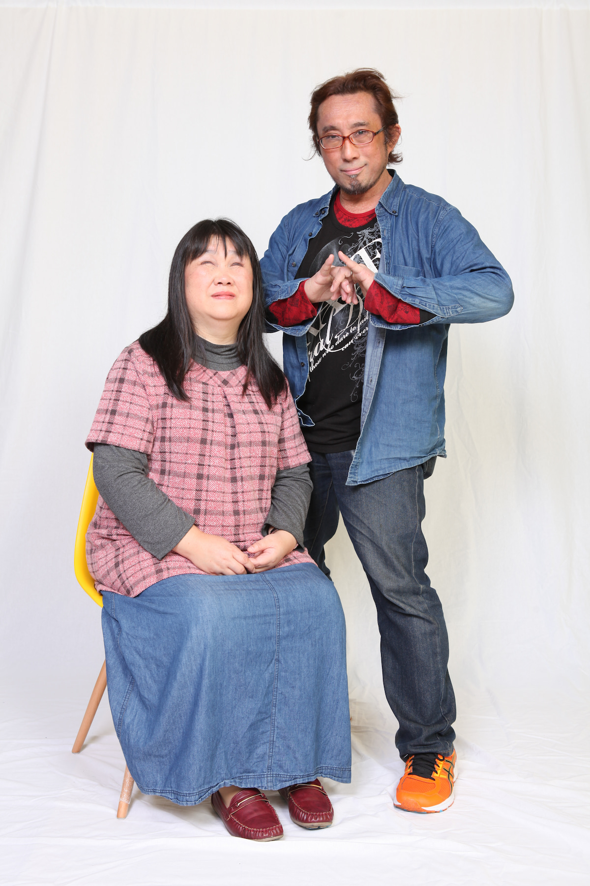 椅子に腰掛けた美月さんと、その横に立つ鈴木さんを写した写真です。鈴木さんは胸の前で、両手の指を絡ませています。左隣にいる美月さんは、両手を膝の上に置き、優しく微笑んでいます