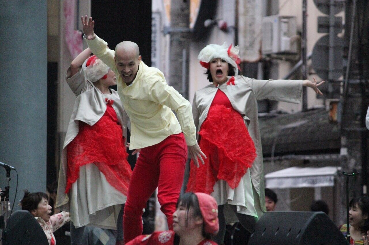 コンテンポラリーダンスをしている澁谷さんと2人のダンサーの写真。いずれも赤と白を基調とした衣装を身に着け、思い思いのポーズを取って踊っている