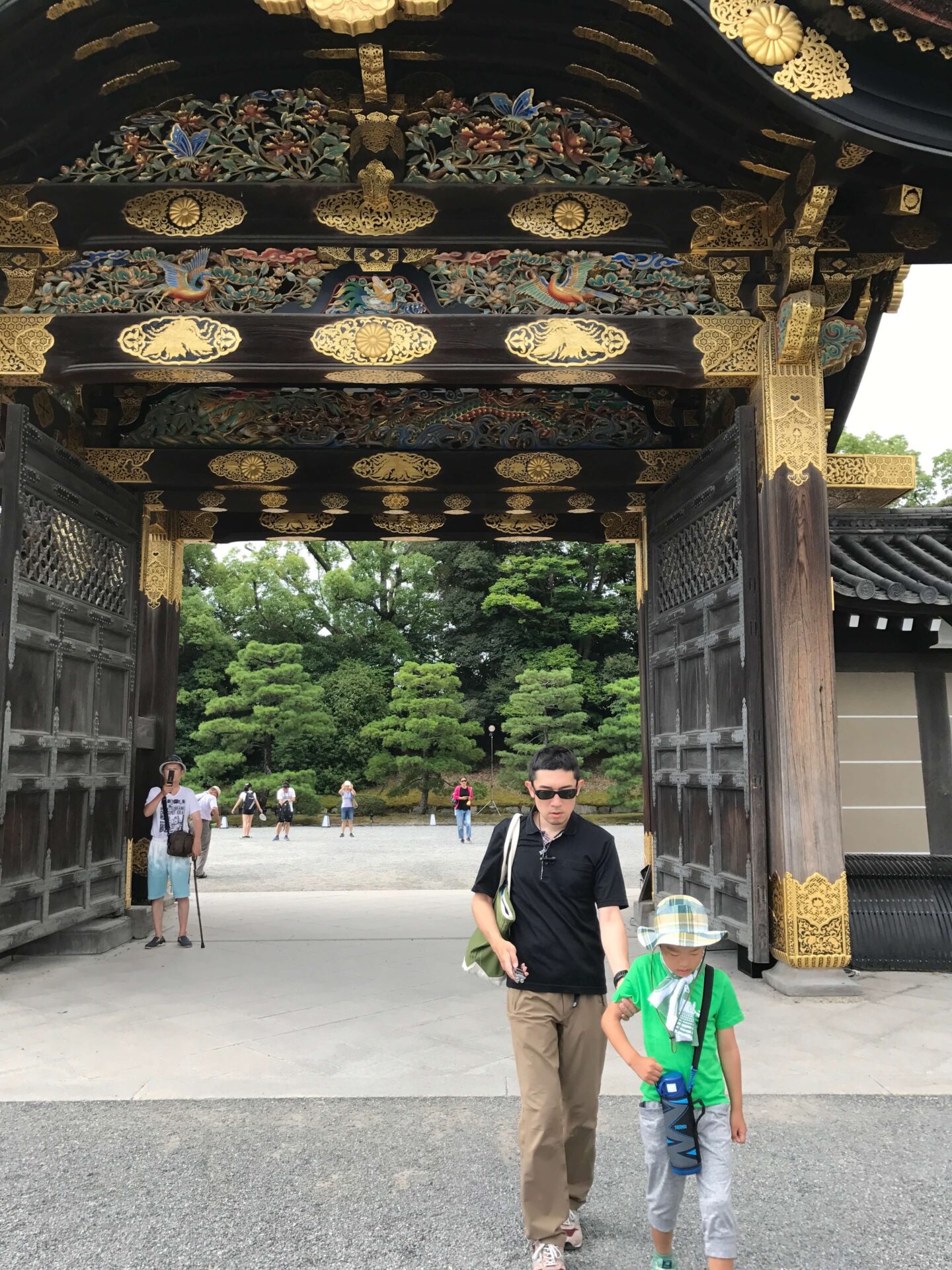竹浪さんが、竹浪さんの息子さんと共に、二条城を散策した際のお写真です。サングラスをかけ目をつむった竹浪さんが、息子さんの肘に手をかけ先導されながら、二条城の門をくぐっています